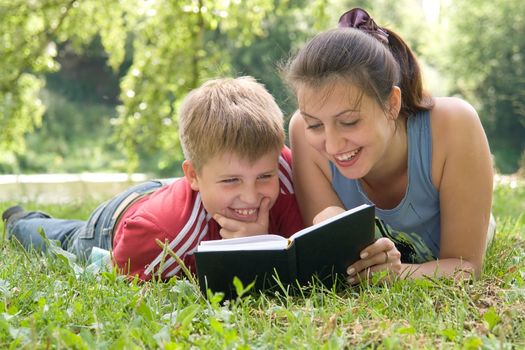 Mum and the son reads the book on a lawn in park