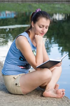 girl reads the book with river at background