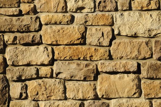 Irregular yellowish masonry block wall surface in sunlight