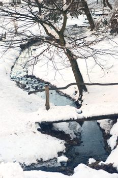 Wooden bridge over small frozen brook covered with snow