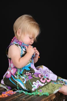 Beautiful blond toddler sitting on an antique trunk playing with beads