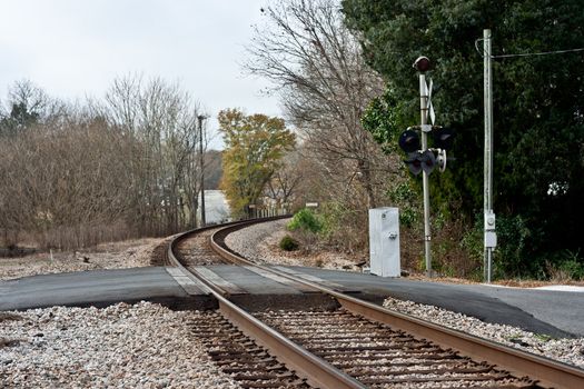 Train crossing with light pole and black pavement.