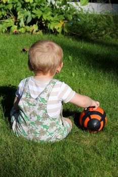 Cute blond baby boy sitting outside in the garden