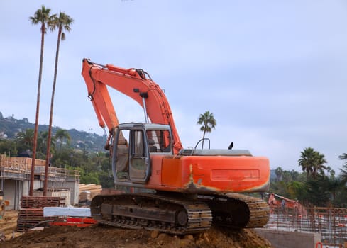 An orange excavator sets on a mound of dirt at construction site