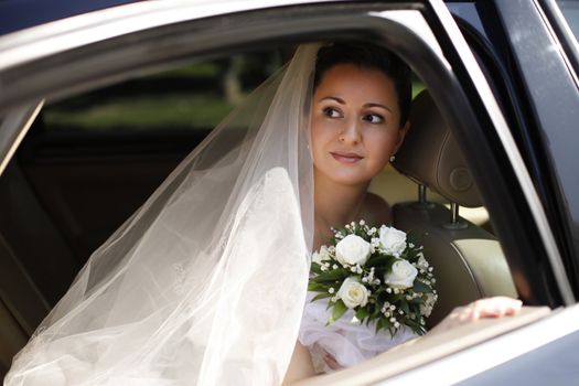 The beautiful bride with bouquet in car