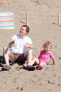 Father and daughter flying kite on the beach on sunny day.