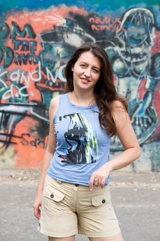 Beautiful young woman in front of graffiti covered wall.