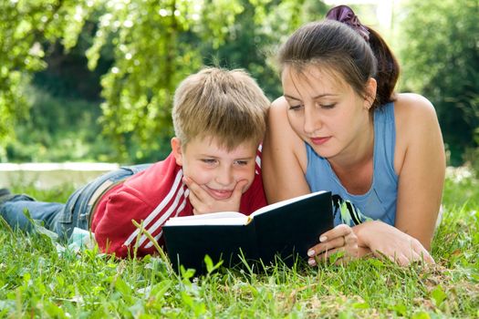 Mum and the son reads the book on a lawn in park