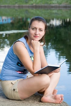 girl reads the book with river at background
