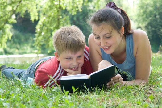 Mum and the son reads the book on a lawn in park