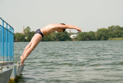 The little boy jumps from a pier in water