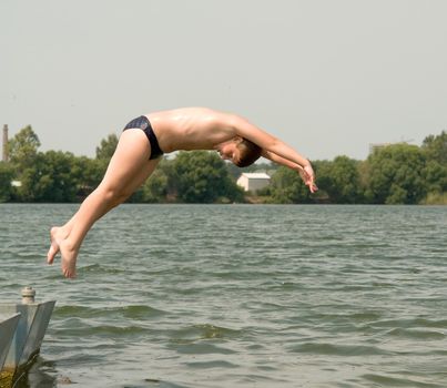 The little boy jumps from a pier in water