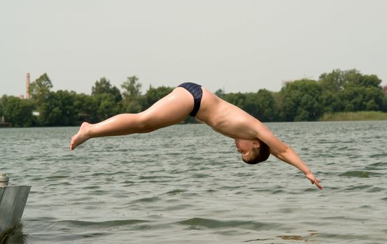 The little boy jumps from a pier in water