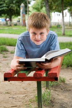 schoolboy reads the book on a bench in park