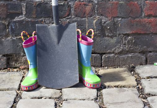 Childs wellington boots and shovel against an old brick wall