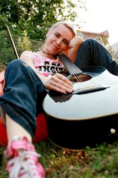 Passionate girl sitting on the grass with a classic guitar in her hands.