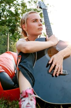Passionate girl sitting on the grass with a classic guitar in her hands.