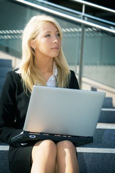 Young businesswoman using laptop computer in city, sitting on stairway