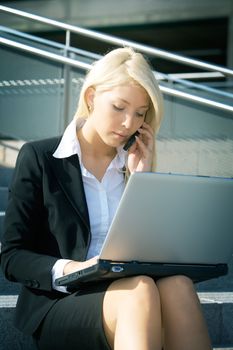 Young businesswoman using laptop computer in city, sitting on stairway