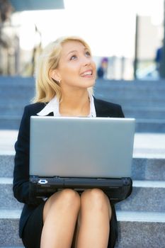 Young businesswoman sitting on stairway, using laptop computer, looking up