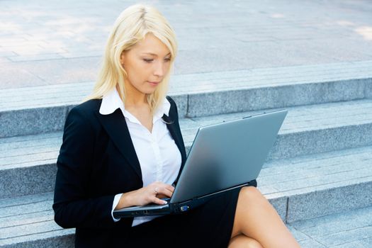 Young businesswoman sitting on stairway, using laptop computer