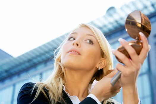 Businesswoman applying make-up outdoors in city, low angle view