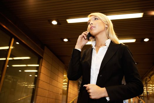 Young businesswoman using mobile phone in passageway of office building