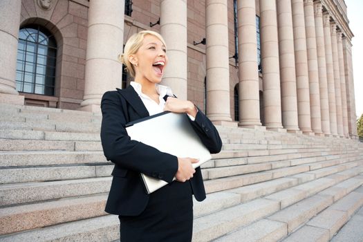 Happy young businesswoman holding laptop computer outside building