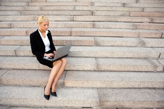 Young businesswoman working with laptop computer, sitting on stairs