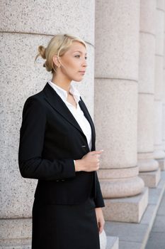 Young businesswoman standing by colonnade pillar, looking away