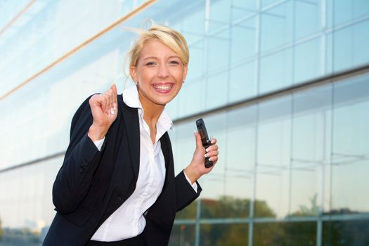 Young businesswoman looking at camera outside office building, holding mobile phone