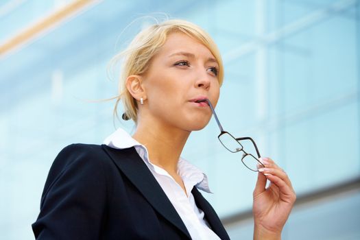 Young businesswoman contemplating outside office building, holding eyeglasses