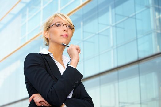 Young businesswoman contemplating outside office building, holding pen