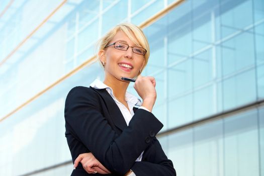 Young businesswoman holding pen outside office building, looking at camera