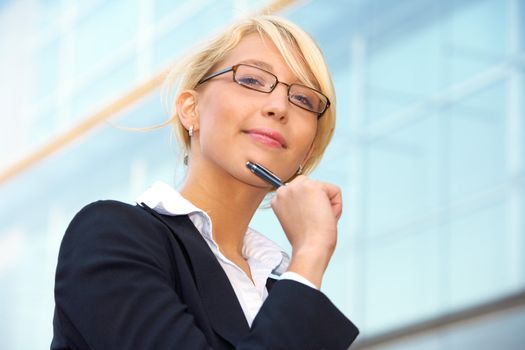 Young businesswoman looking at camera outside office building, holding pen