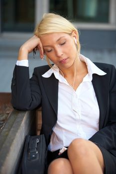 Young businesswoman sitting on bench wearing earphones with eyes closed