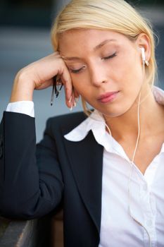 Young businesswoman wearing earphones with eyes closed, holding eyeglasses