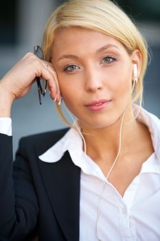 Young businesswoman wearing earphones looking at camera, holding eyeglasses