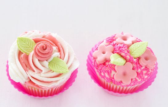 Vanilla cupcakes with buttercream icing and pink flower decorations on white background