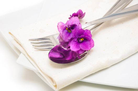 A spoon with a fork on a napkin and a plate decorated with violets