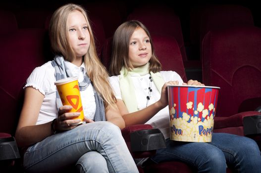 two girls look three-dimensional cinema, sitting in the glasses, eat popcorn, drink drink