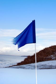 a snow covered links golf hole in ireland in winter weather with blue flag