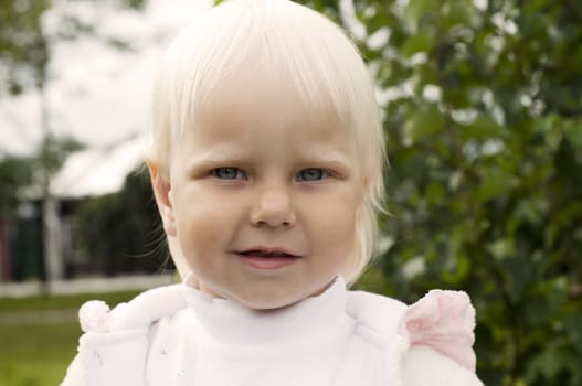 portrait of a young blond girl in white dress, poses in the park