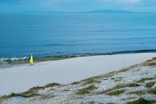 a snow covered links golf hole in ireland in winter weather with yellow flag