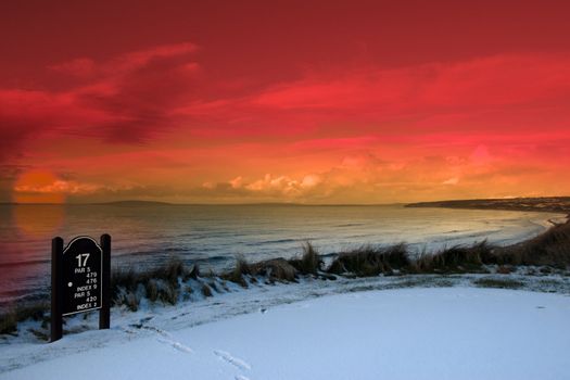 a snow covered links golf hole in ireland with seventeen tee sign and orange sunset sky