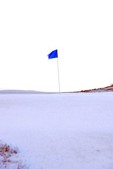 a snow covered links golf hole in ireland in winter weather with blue flag