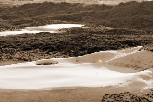 a snow covered links golf hole in ireland in winter weather with yellow flag in sepia