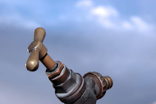 an outdoor water tap against a blue cloudy sky