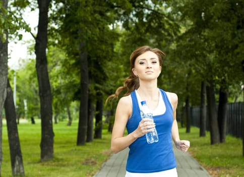 young woman jogging in the park in summer, trees and grass background