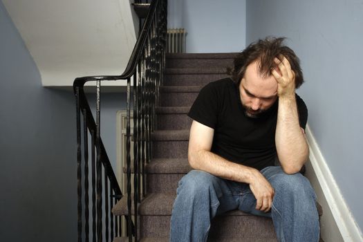 A male adult with serious depression sitting in the stairwell of his apartment building.
